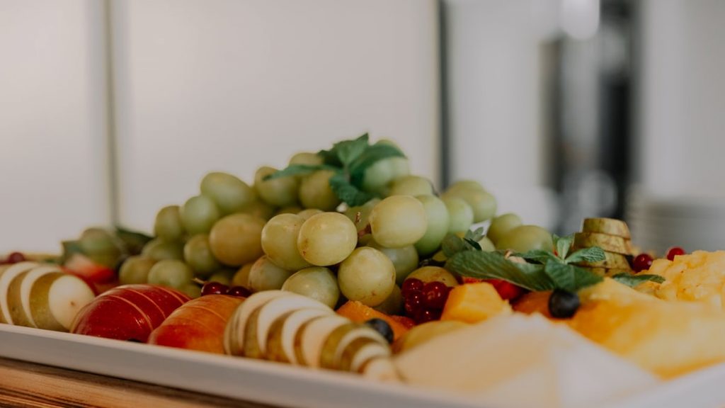 A vibrant assortment of fruits including grapes, apples, and berries on a white tray.